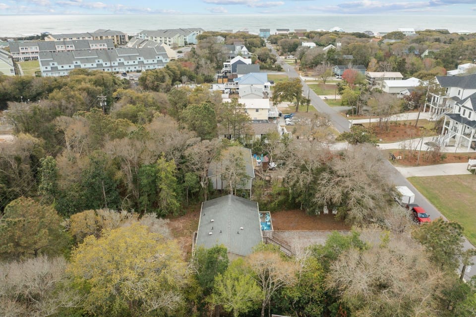 Aerial view of a coastal residential area with mature trees and nearby accommodations, showing the peaceful neighborhood setting.