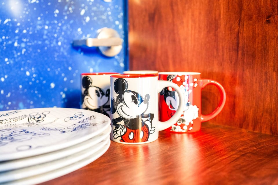 A set of mickey and minnie mouse mugs and plates displayed on a wooden shelf.