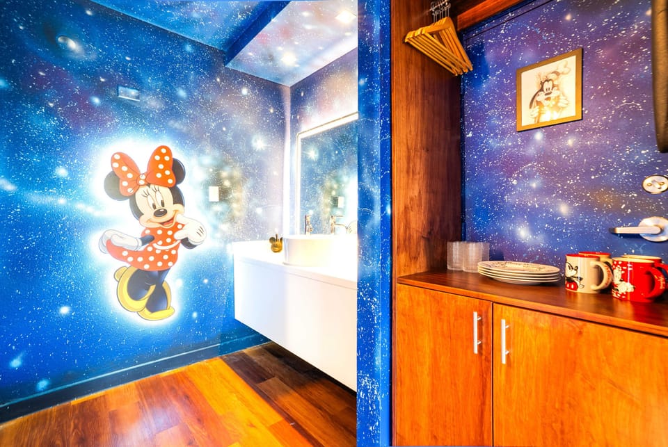 A vibrant space featuring a galaxy-themed wall with a large Minnie Mouse illustration and wooden cabinetry with Disney-themed mugs and plates.