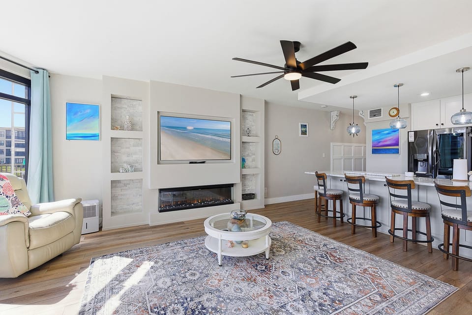 Experience a relaxing beach stay in this open-concept living area featuring a cozy fireplace, coastal décor, and spacious kitchen bar seating. Bright, airy, and perfect for gathering after a fun day at the beach.