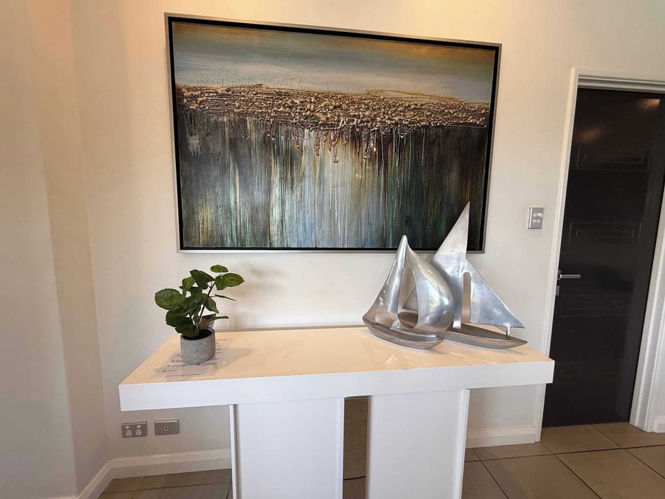 Experience the charm of our space! A textured painting sets the mood, a serene green plant and a magnificent silver sailing figurine. Relax in an environment where every detail is designed for your comfort and style.