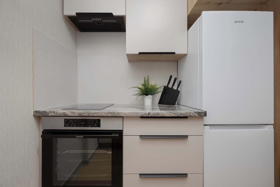 A streamlined kitchen wall features a tall white refrigerator and a built-in oven. The white cabinetry and light backsplash keep the small space feeling open and clean.