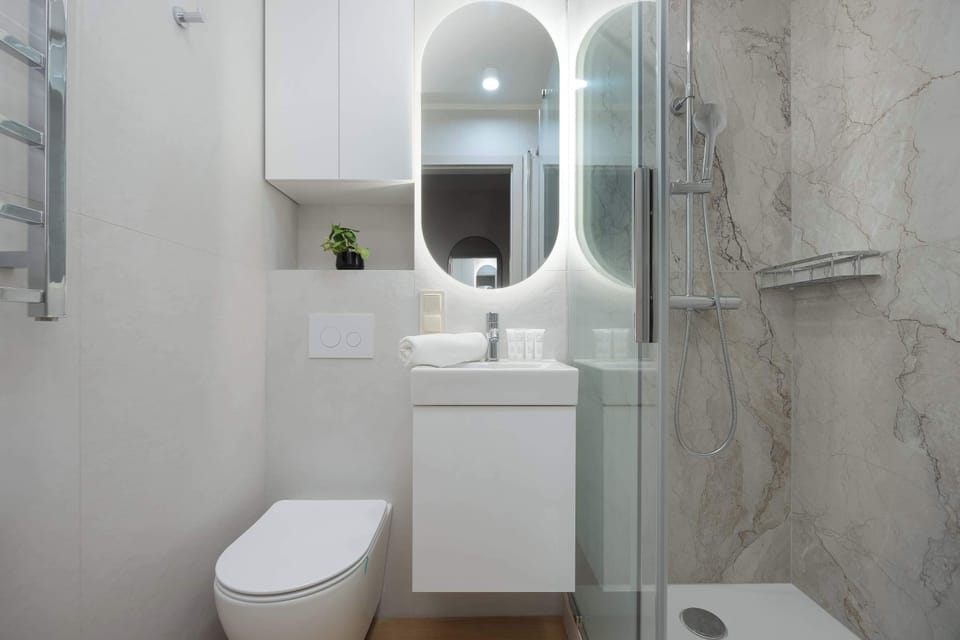 A sleek bathroom features a backlit circular mirror above a white vanity unit. The grey marble-effect tiles on the walls give the room a high-end, contemporary feel.