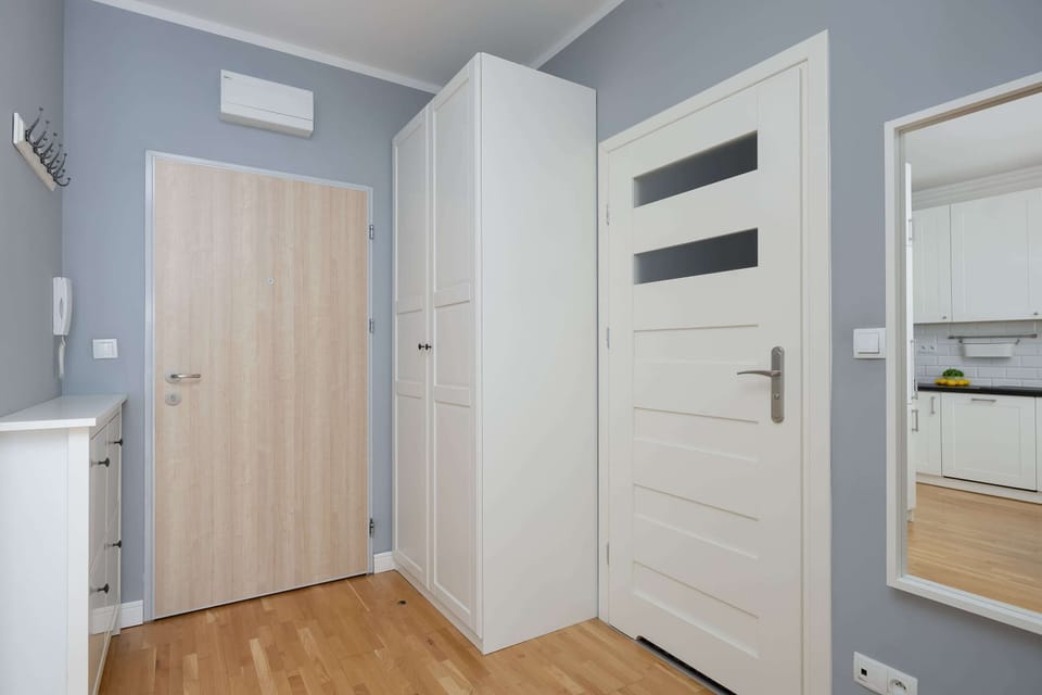 A corridor with built-in wardrobes and mirrors, providing storage and depth. The bright flooring and white walls enhance the sense of space.