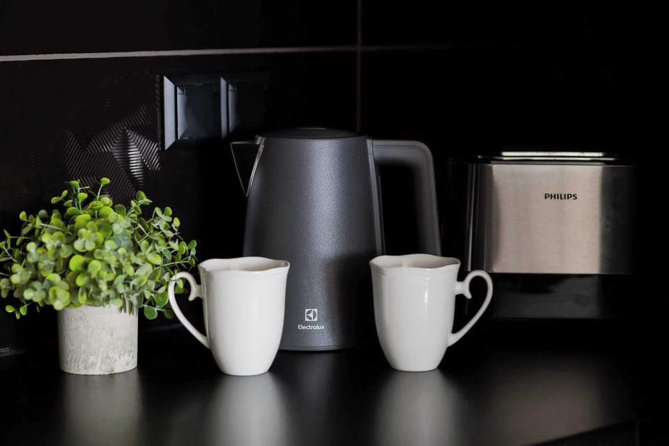 A focused shot displays a modern black kettle, toaster, and two white mugs ready for guest use.