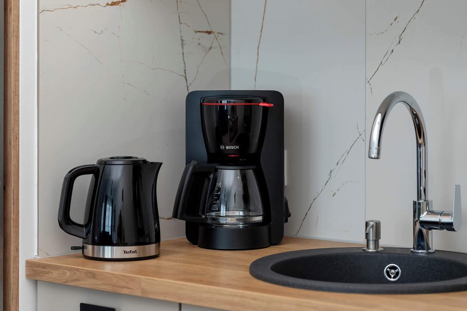 The kitchen sink area shows a stainless steel sink with a high-neck faucet, next to a black electric kettle and a drip coffee machine.