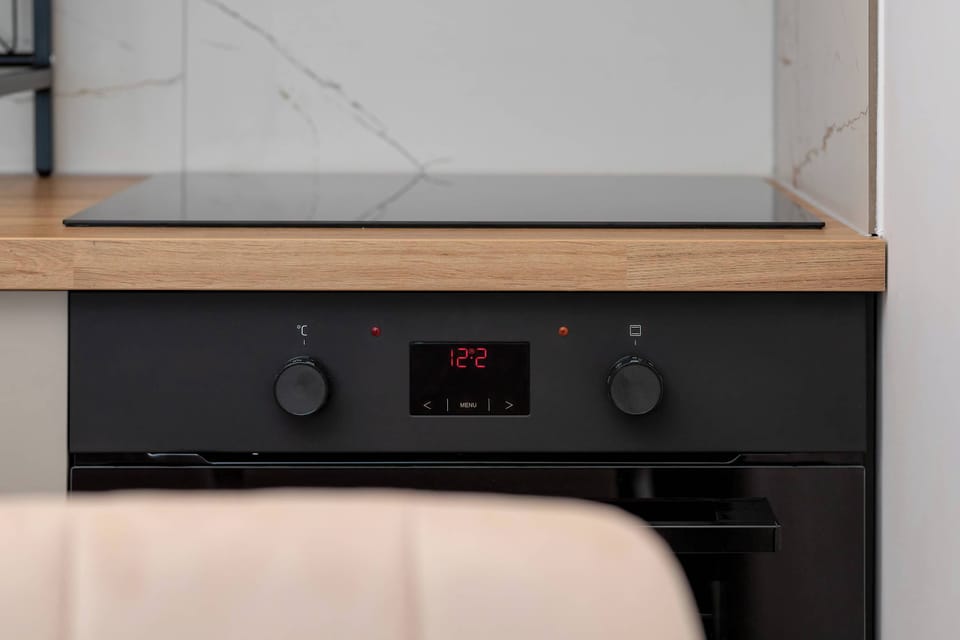 A detailed view of a black electric oven with a digital clock and control knobs, integrated below a light-wood countertop.