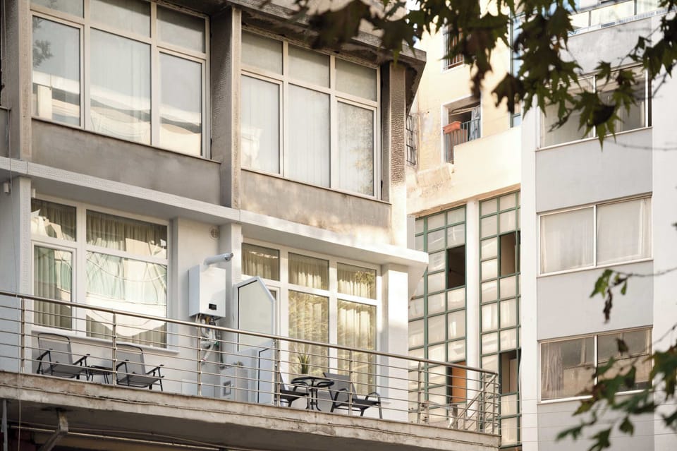 Balcony view facing nearby buildings and trees, with railings and urban surroundings visible, offering a glimpse of the neighborhood.


