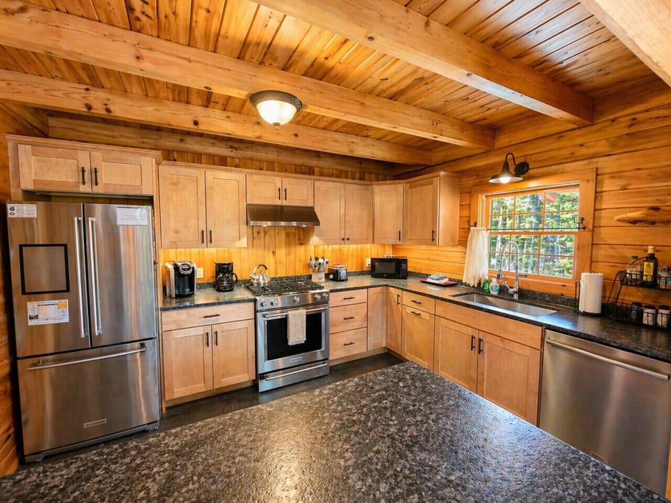 Modern log cabin kitchen with stainless steel appliances, rustic wood interiors, and warm natural light.