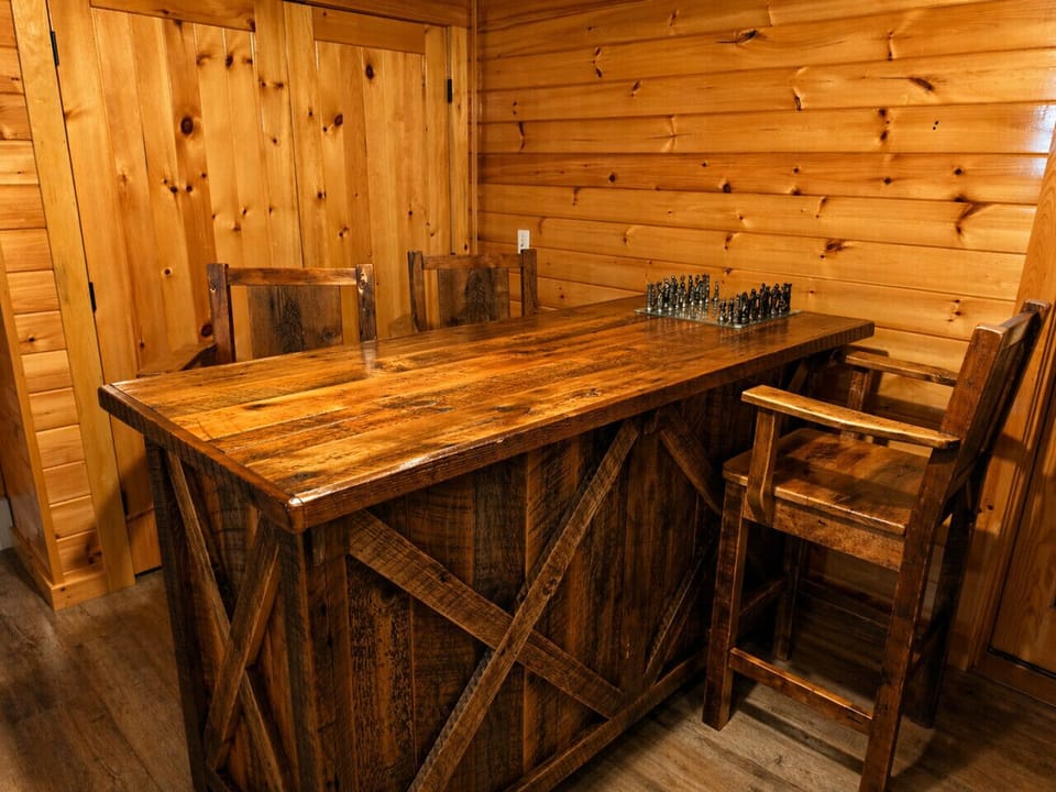 Rustic game room with a handcrafted wood table, bar seating, and classic chess for cozy cabin nights.