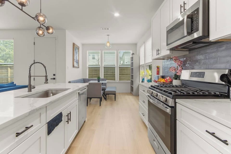 Fully equipped kitchen with stainless steel appliances, gas stove, microwave, spacious countertops, and a dining area just steps away.