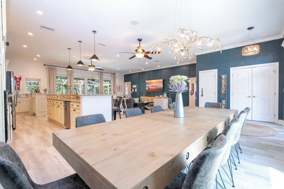 Enjoy meals in this spacious dining area with a beautiful wooden table for eight and cozy black chairs. Large windows let in natural light, enhancing the vibrant blue walls and stylish light fixtures for a welcoming atmosphere.