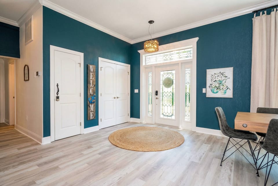 Welcome to a bright entryway with rich blue walls that beautifully contrast the light wood flooring. A round jute rug adds warmth, while an elegant light fixture draws your gaze upward, enhancing the spacious ambiance.
