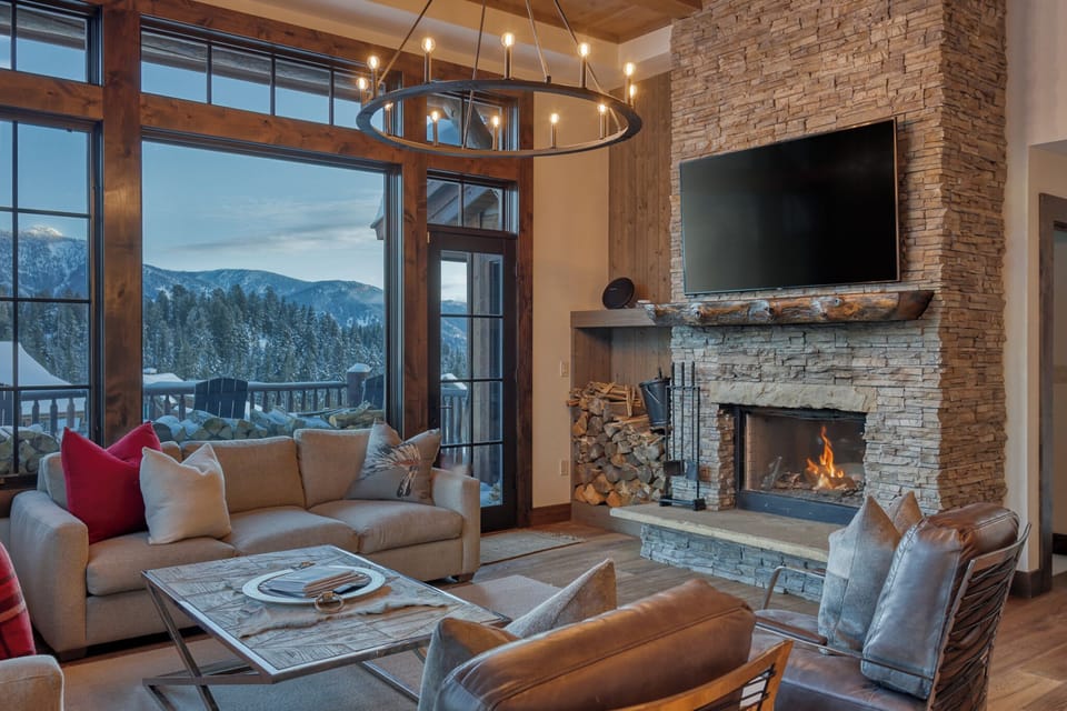 Sink into plush seating by the crackling fireplace while mountain views frame your perfect alpine retreat through floor-to-ceiling windows.