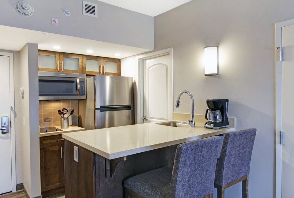 Kitchen counter with bar stools, stainless steel fridge, microwave, glass-front wood cabinets, and a coffee maker — bar seating for two.