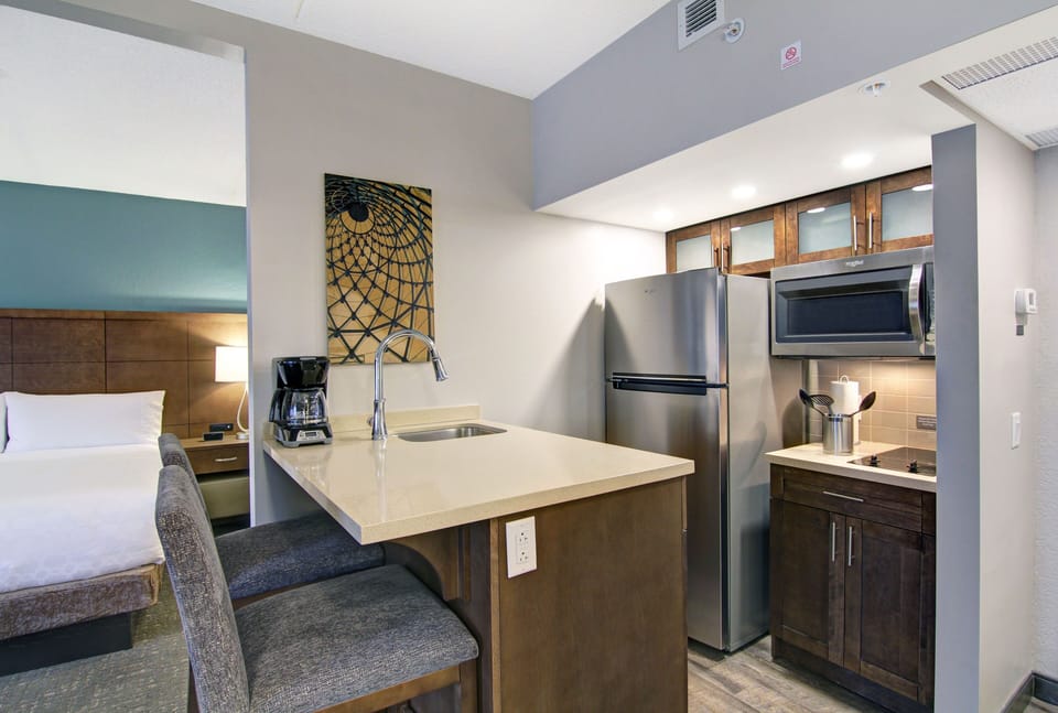 Fully equipped kitchen with stainless steel appliances, glass-front wood cabinets, and bar seating for two.