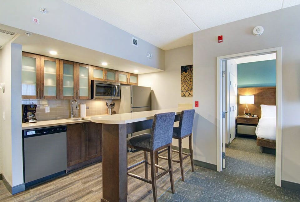 Dark wood and glass-front kitchen cabinets with stainless steel appliances — counter extends into a kitchen bar for in-suite dining.