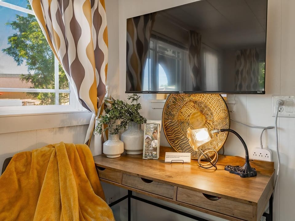 Wood desk with three drawers holds ceramic vases, a patterned plate, and a vintage-style lamp beneath a wall-mounted TV.