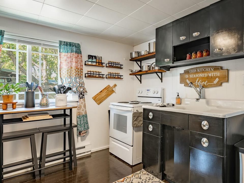 Black cabinetry and white appliances frame the kitchen, with open wood shelves holding stainless pots and jars.