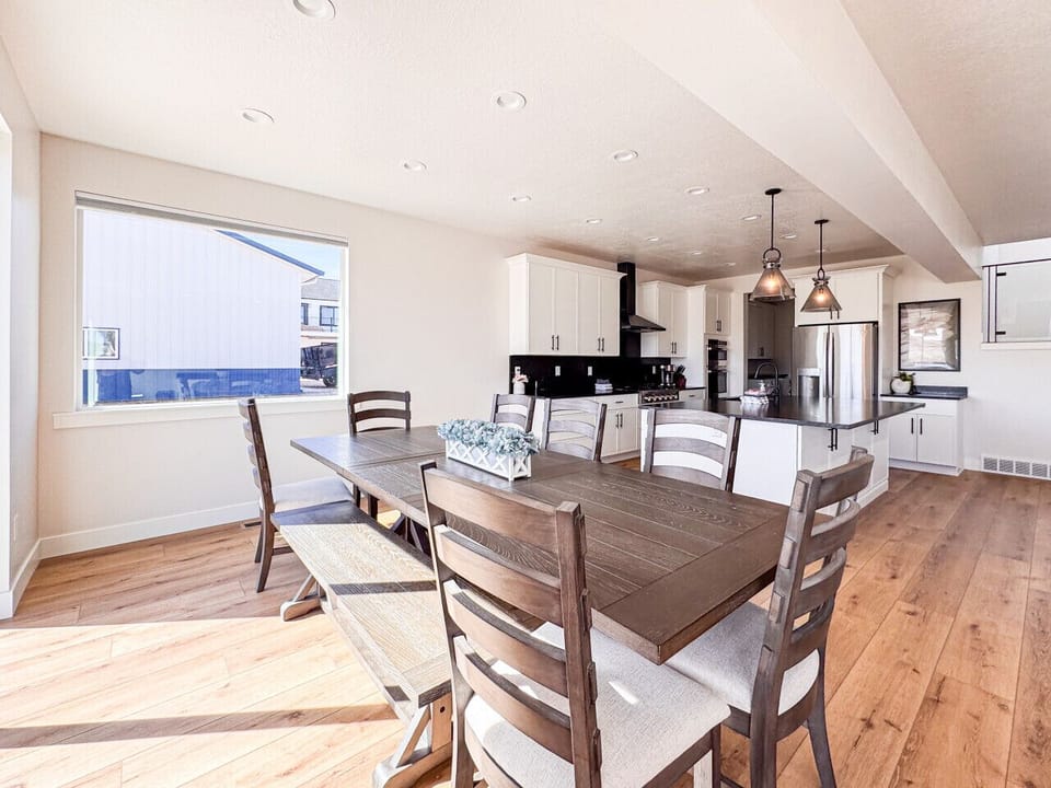 Modern kitchen and dining area with natural light, wood table, and sleek white cabinetry