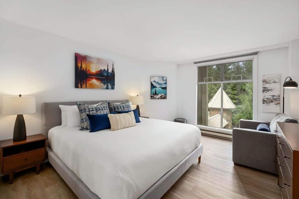 - Peaceful bedroom with soft lighting and forest-view window for serenity - Crisp white linens and modern furnishings create a relaxing retreat - Cozy setup for restful nights after exploring Whistler’s mountain trails