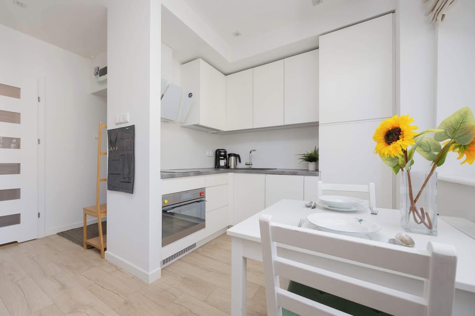 A wider angle of the compact kitchen shows all appliances, including the built-in stovetop and oven. A chalkboard hangs on the wall, and the window sill is decorated with two potted plants.