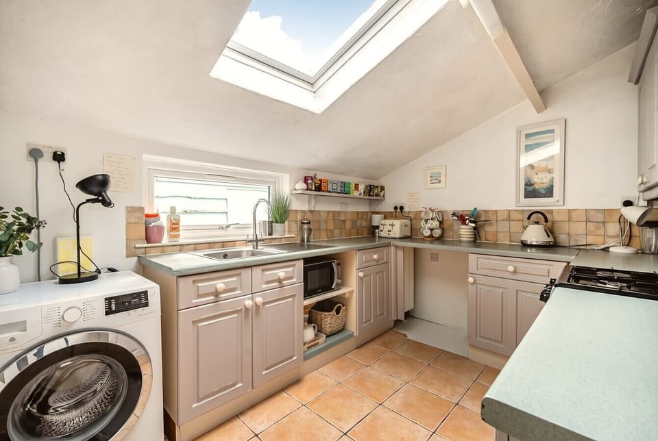 Bright skylit kitchen with gas hob, microwave and washing machine.