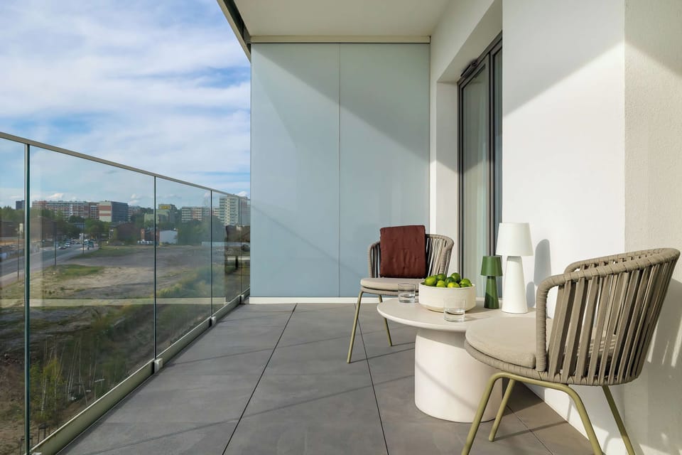 A bright balcony with outdoor seating and glass railings overlooking the area.