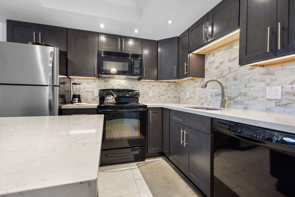 Your sleek modern kitchen features dark cabinetry, stone countertops, and premium appliances—perfect for preparing meals at home.
