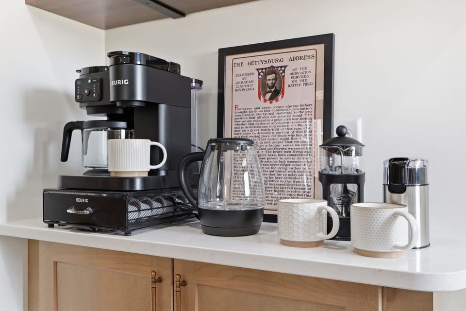 Morning briefing before the battlefield tour — Keurig, French press, electric kettle, and the Gettysburg Address watching over it all. Fourscore and seven cups of coffee.