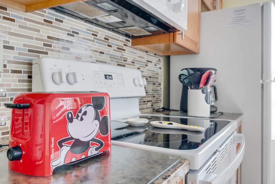 A kitchen countertop featuring a red Mickey Mouse toaster and a white electric stove with a glass cooktop.