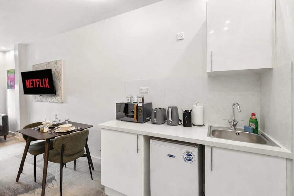 Compact yet stylish kitchenette featuring sleek white units, sink, fridge, microwave, kettle and toaster. Perfectly equipped for preparing light meals, with a modern finish that blends seamlessly into the open-plan living and dining space