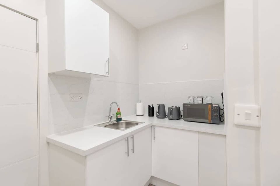 Compact yet stylish kitchenette featuring sleek white units, sink, fridge, microwave, kettle and toaster. Perfectly equipped for preparing light meals, with a modern finish that blends seamlessly into the open-plan living and dining space