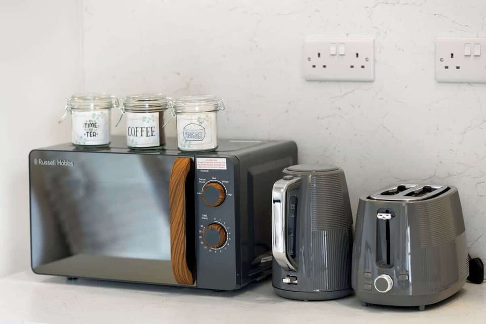 Compact yet stylish kitchenette featuring sleek white units, sink, fridge, microwave, kettle and toaster. Perfectly equipped for preparing light meals, with a modern finish that blends seamlessly into the open-plan living and dining space