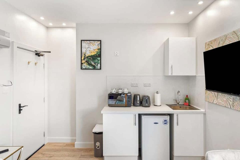 Compact yet stylish kitchenette featuring sleek white units, sink, fridge, microwave, kettle and toaster. Perfectly equipped for preparing light meals, with a modern finish that blends seamlessly into the open-plan living and dining space
