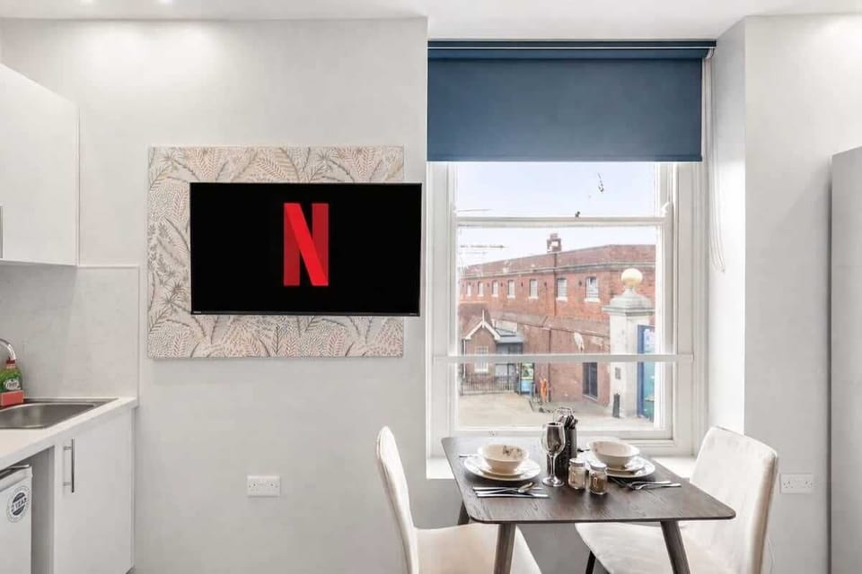 A stylish open-plan dining space with a sleek wall-mounted Smart TV and elegant seating for two. Bathed in natural light from the large window, offering charming city views—perfect for relaxed breakfasts or cosy evenings with Netflix.