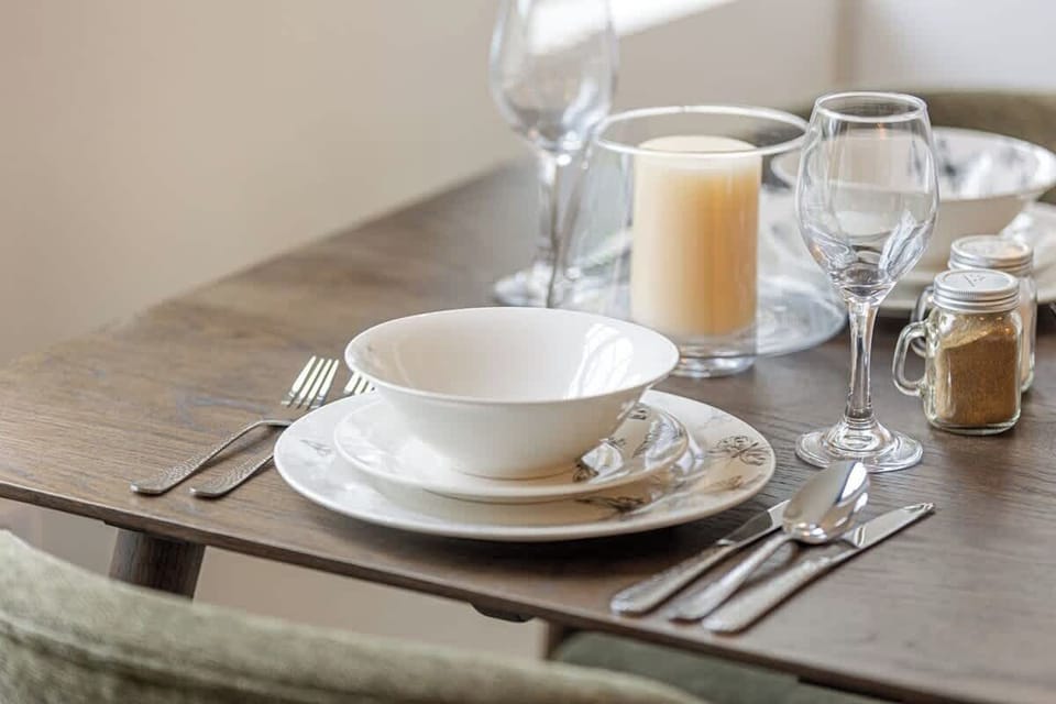 An intimate dining space set for two, perfect for relaxed breakfasts or cosy evening meals. Positioned beside large windows, natural light fills the area, creating a calm and stylish setting to dine and unwind.
