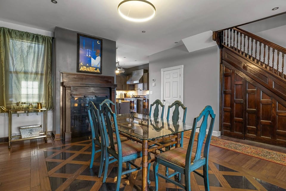 Dining table, Café Arabica art above the fireplace, kitchen beyond, grand staircase on the right, and the brass bar cart ready to go.