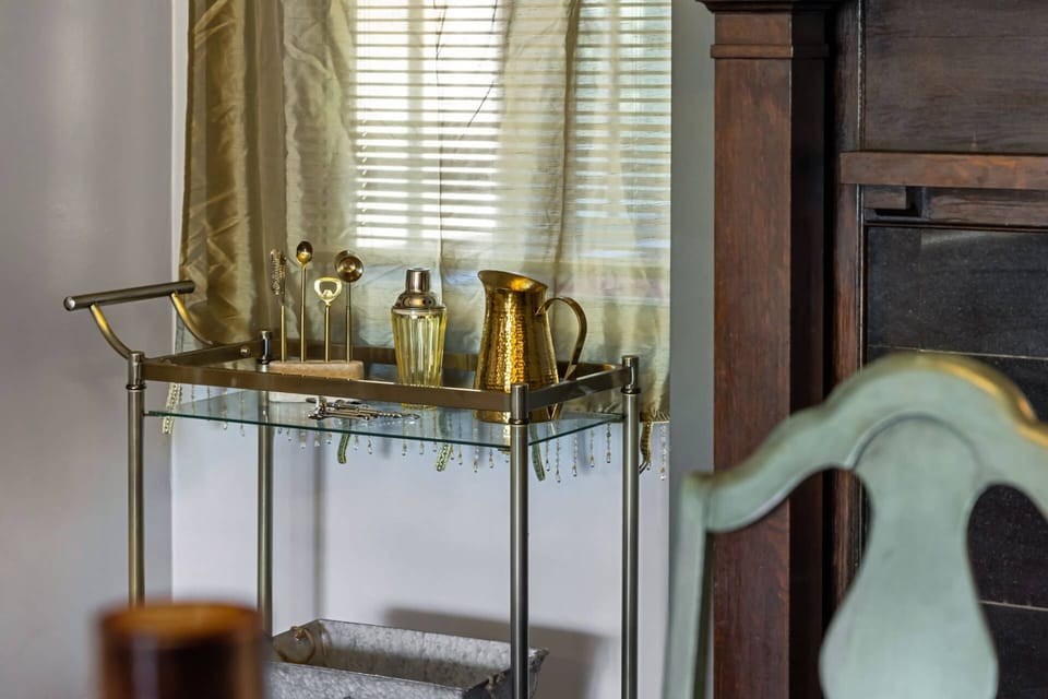 A polished brass bar cart stocked with cocktail shaker, hammered gold pitcher, and bar tools — cocktail hour starts here.