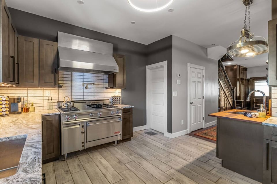 The commercial range, range hood, and island — with the hallway and original staircase visible beyond. Space and function in one.