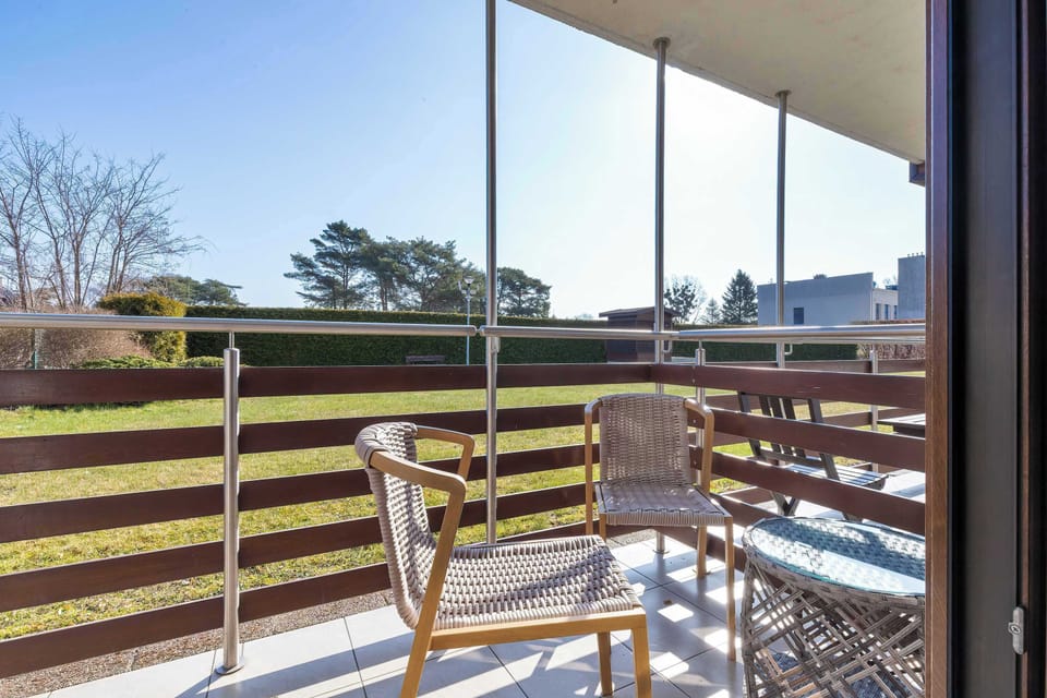A balcony with wooden flooring and outdoor seating, overlooking a residential area. The space is perfect for relaxing outdoors in fresh air.