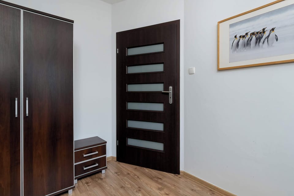A bedroom featuring a spacious wardrobe with modern doors and a wooden floor. The storage space is practical and blends well with the clean, minimalist interior.
