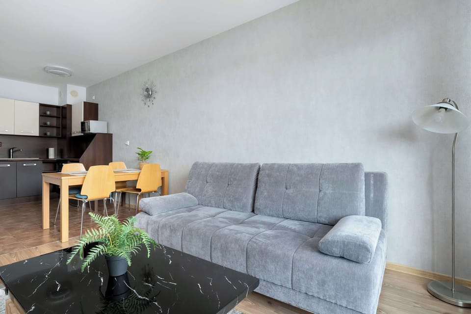 A cozy living space with a sofa and a small coffee table, decorated with flowers. The interior design is simple and inviting.