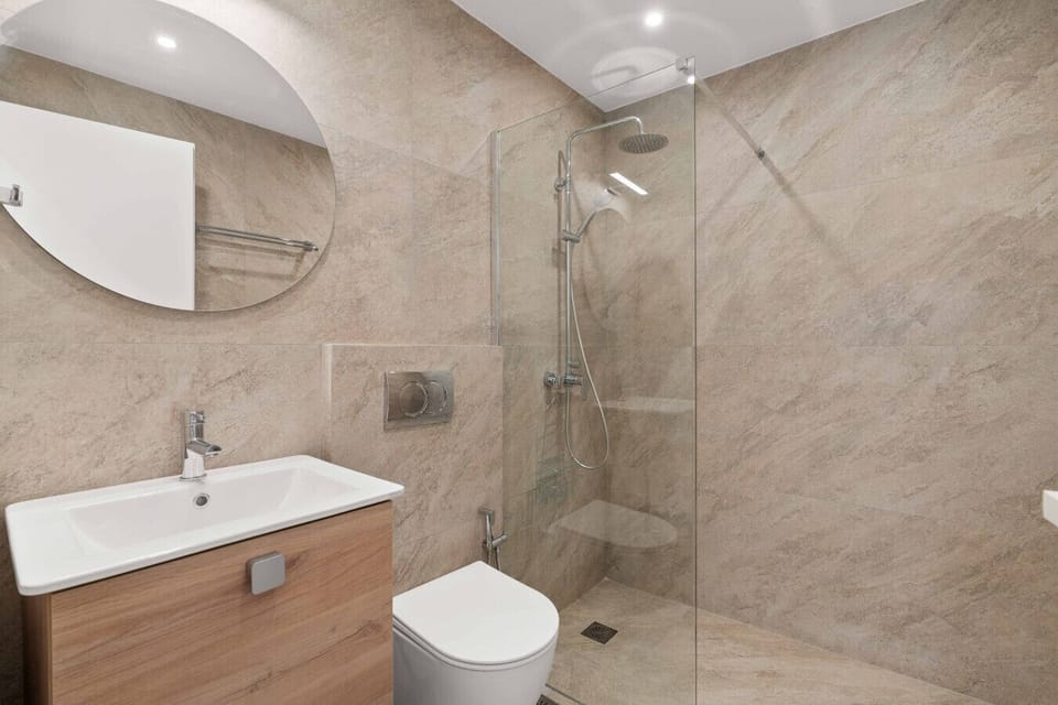 Full bathroom with walk-in shower, stone-finish walls, round mirror, and quality fittings.