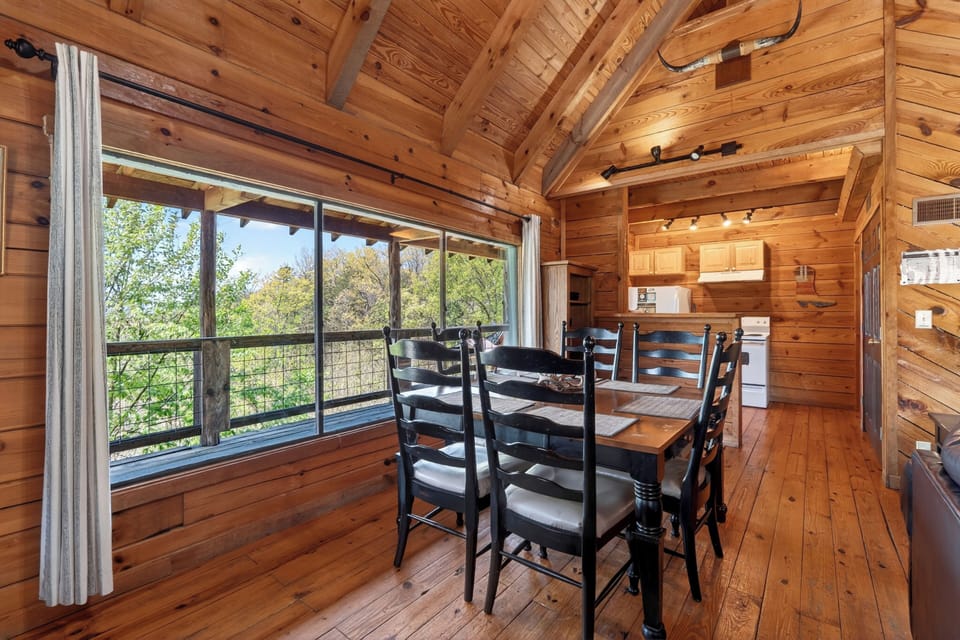 Rustic cabin dining room with warm wood beams, a sturdy farmhouse table, and big windows opening to peaceful forest views.