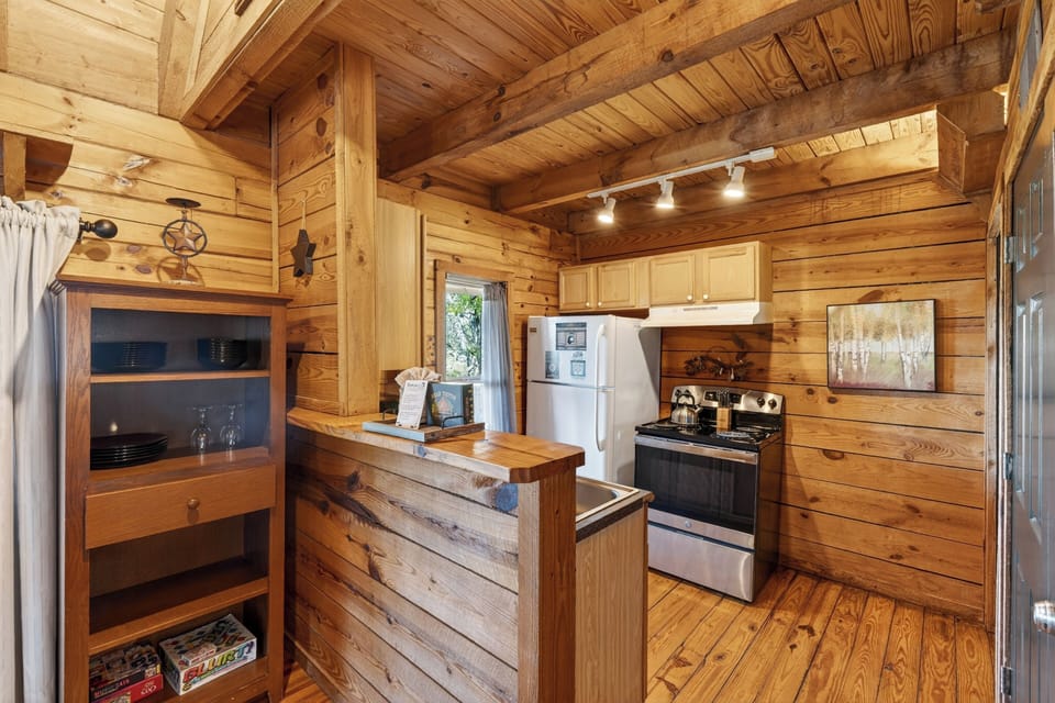 Warm wood‑paneled cabin kitchen with simple comforts, soft lighting, and a cozy rustic charm.