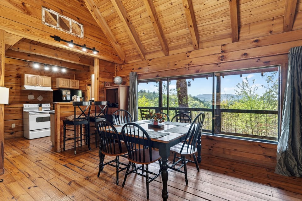 Warm wood‑paneled cabin dining room with a rustic table, mountain views through large windows, and soft natural light filling the space.