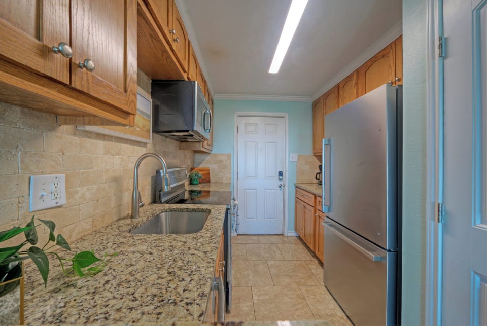 Fully equipped kitchen with granite countertops and stainless steel appliances, opening to a bright living space with ocean views.