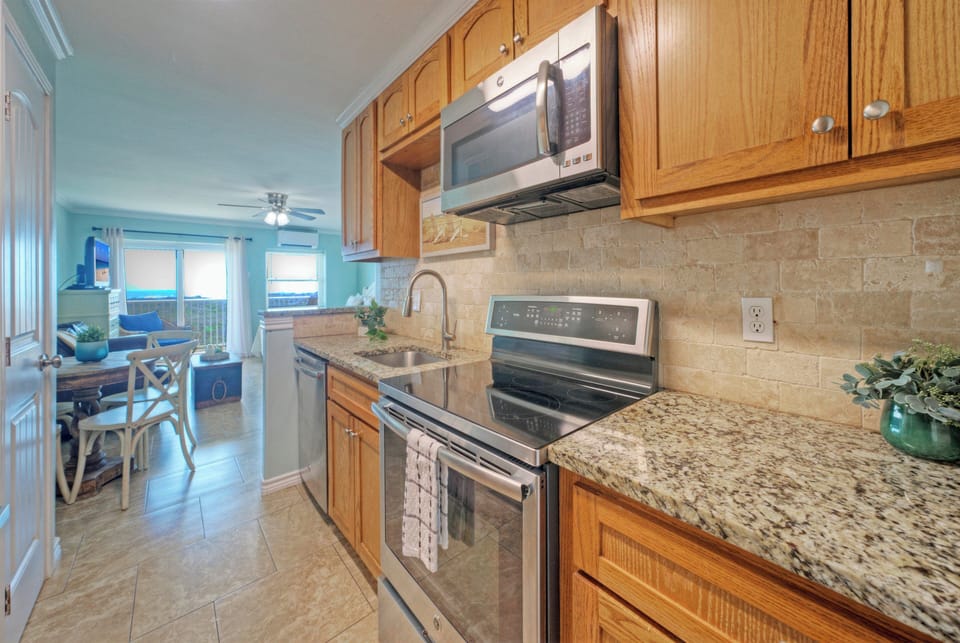 Fully equipped kitchen with granite countertops and stainless steel appliances, opening to a bright living space with ocean views.