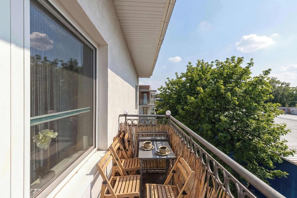 A balcony view with outdoor seating overlooking greenery and neighboring buildings.